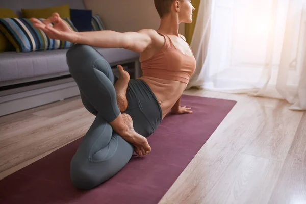 Hermosa mujer joven haciendo ejercicio en casa, haciendo ejercicio de yoga en la estera púrpura, ejercicio de equilibrio de brazos con piernas cruzadas — Foto de Stock