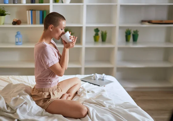 Sidovy på charmig kaukasisk kvinna med kopp te på sängen — Stockfoto