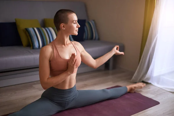 Белая женщина дома практикует йогу, делает сплит — стоковое фото