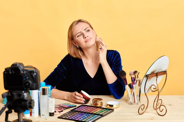 Dissatisfied female cosmetics expert applies face cream on cheek, frowns in dislike — Stock Photo, Image