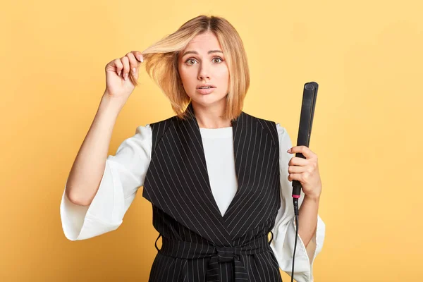 Distracted female hair stylist poses with curling iron, cant make hairdo