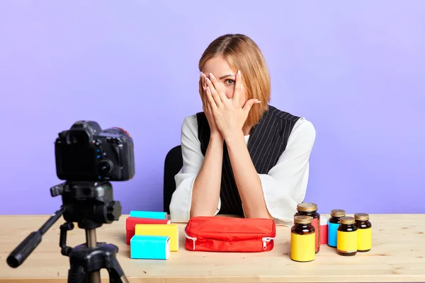 Tired female model closes her face with hands, keep an eye on camera