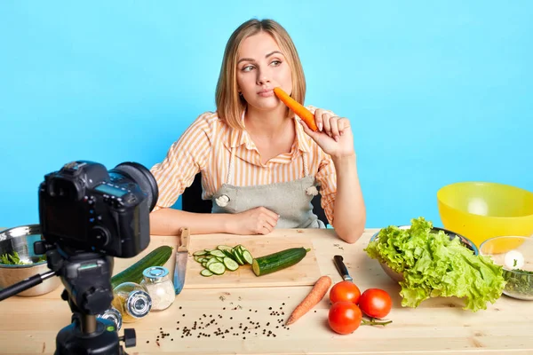 Přemýšlivý ženský blogger, který drží čerstvou mrkev a přemýšlí, co bude vařit dál — Stock fotografie