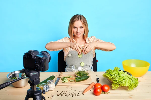 Yetenekli kadın aşçı sağlıklı yemek yapıyor, salatalıkları kaseye atıyor. — Stok fotoğraf