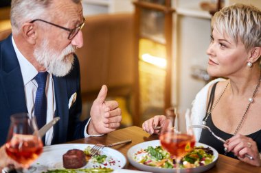 Güzel bayan ve yaşlı adam restoranda dostça sohbet ediyorlar.