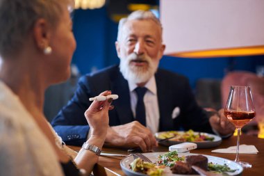 Üst düzey Kafkasyalı çift lokantada yemek yerken sohbet ediyorlar.