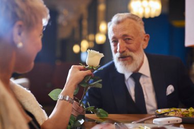 Sevgi dolu bir adam kadınına beyaz çiçek sunar. Restoranda yıldönümü kutlayan çift