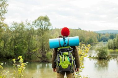 Genç kaşif bir peri masalı manzarasının önünde nehir kıyısında duruyor.
