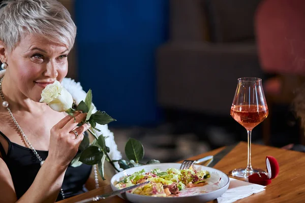 Mulher sênior loira elegante com rosa linda olhar para o marido no restaurante — Fotografia de Stock