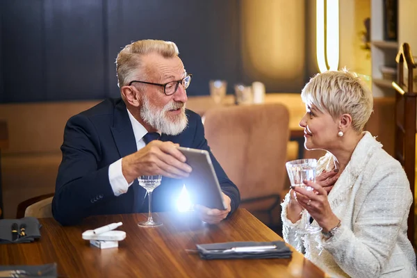 Κοίτα εδώ. Senior ώριμο ζευγάρι κάθεται στο εστιατόριο και μιλώντας, ενώ ο άνθρωπος δείχνει στο tablet — Φωτογραφία Αρχείου