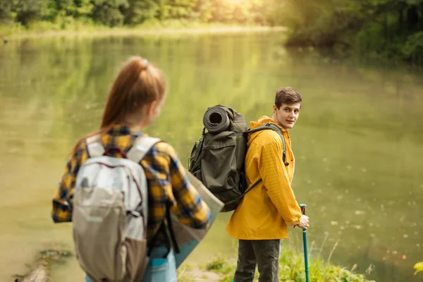 Joven senderista rubia mirando hacia atrás mientras está de pie cerca del lago —  Fotos de Stock