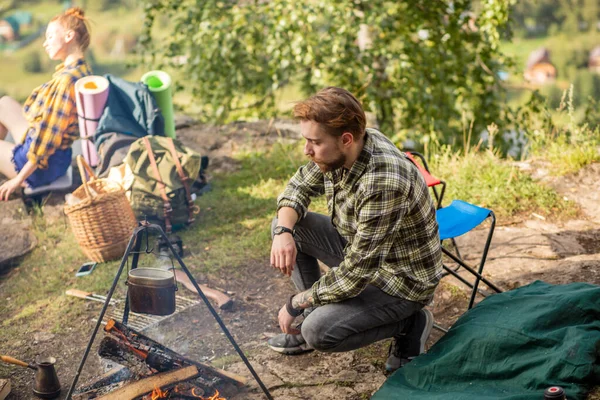 キャンプでたき火の横に座っている若いハンサムな男 — ストック写真