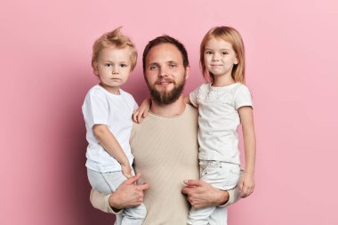 Yakışıklı baba pembe arka planda küçük kızını ve oğlunu taşıyor.