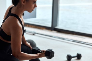 Spor salonunda ağırlık kaldıran genç bir kadın. Kol kasları çalışıyor.