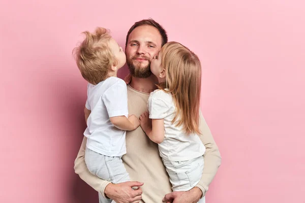 Kleine dochter en zoon zoenen hun vader geïsoleerd over een roze achtergrond — Stockfoto