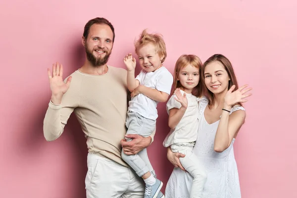 Щаслива молода сім'я з чарівними маленькими доньками позує на рожевому фоні — стокове фото