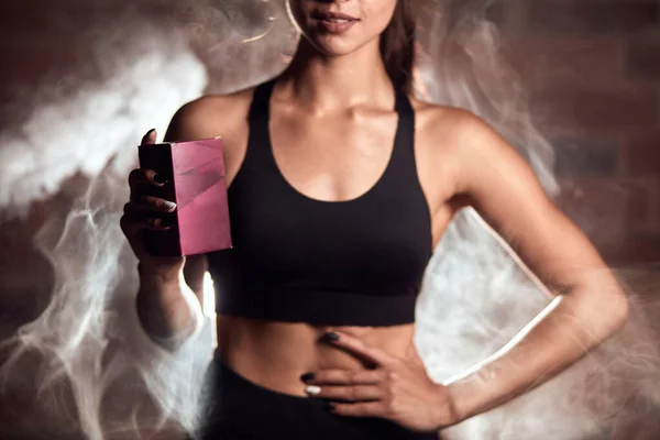 Mujer deportiva de pie en el fondo de vapor, la celebración de farmacia deportiva, alimentos de nutrición —  Fotos de Stock