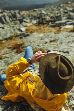 Dürbün kullanan şapkalı ve ceketli genç bir sırt çantalı.