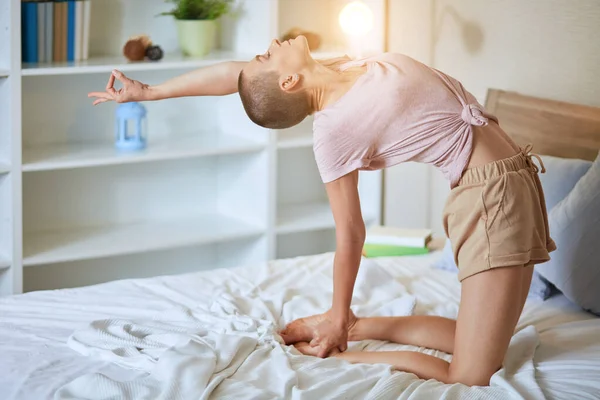 Cute young caucasian girl at morning practicing yoga on white bed — Stock Photo, Image