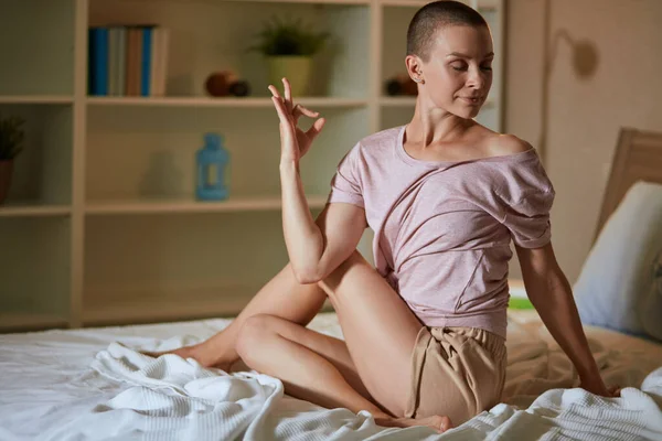 Morgon med ung kvinna som gör yogaövningar i sovrummet på sängen. — Stockfoto