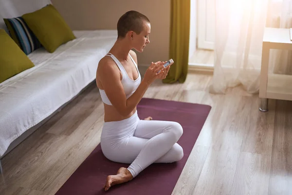 Beautiful sporty woman sitting on purple mat, holding a phone in hands — Stock Photo, Image