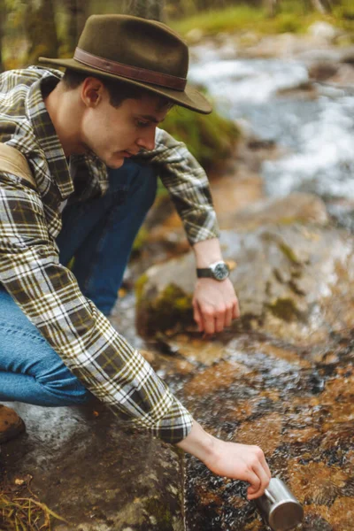 Giovane bel turista in possesso di tazza. . Un uomo che riempie tazza di acqua di fiume . — Foto Stock