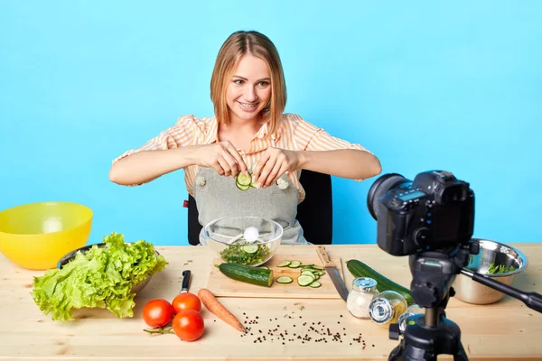 Kuchařka sedí u stolu s produkty, dělá zdravý salát se zeleninou — Stock fotografie