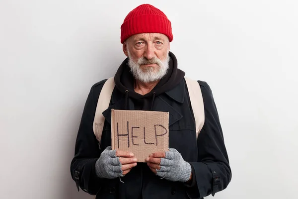 Szegény öreg csavargó piros kalapban és utcai viseletben, kartontáblával a kezében. — Stock Fotó