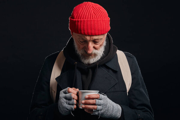 Старший нищий мужчина держит кружку горячего чая для разогрева
