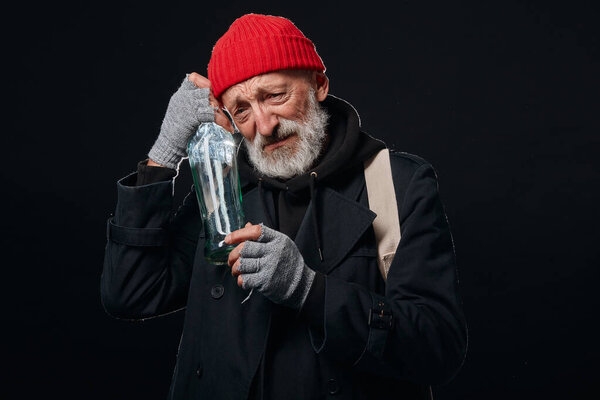 Desperate sad senior homeless man with bottle of alcohol