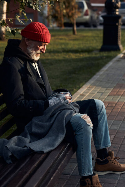 elderly person without home, money and work sitting on bench on street