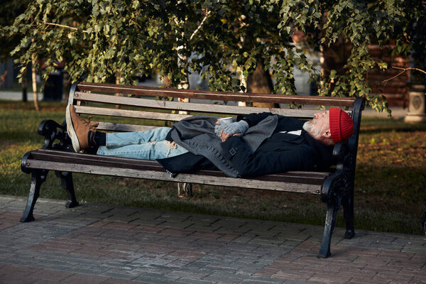 Beggar male sleeping on bench during the day