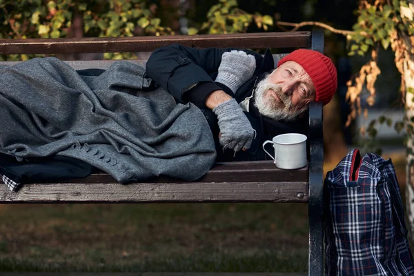 Pobre sem-teto deitado no banco em tempo frio — Fotografia de Stock