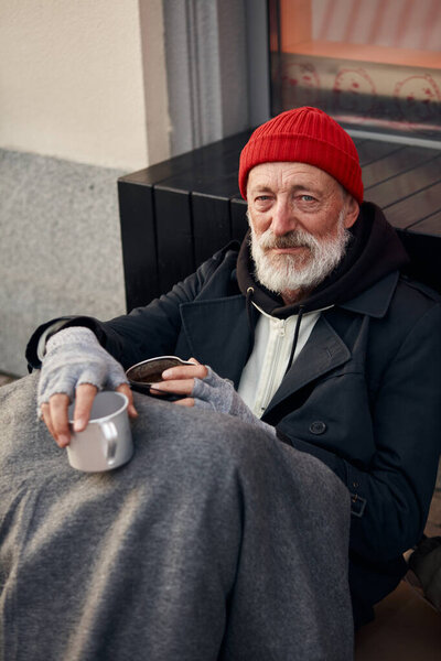Kind mature beggar man with mug begging on city street