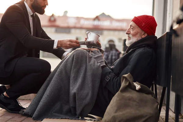 Miłosierny mężczyzna w smokingu pomaga bezdomnemu. — Zdjęcie stockowe