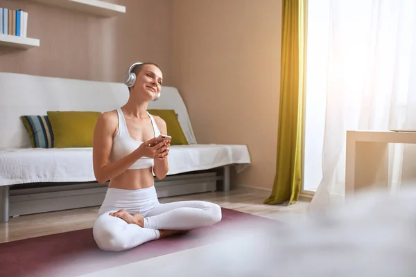 Glada kaukasiska unga korthåriga kvinna sitta på mattan hemma och lyssna på musik med hörlurar — Stockfoto