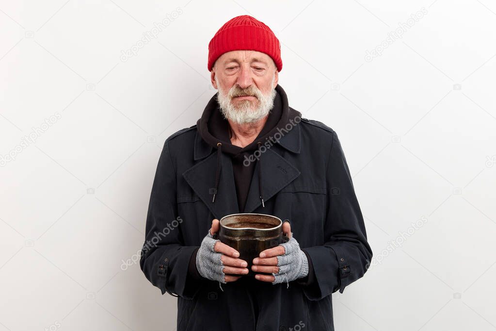 Old homeless man with grey beard in black coat holding iron can for money
