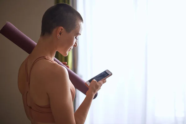 Jovem caucasiano carregando um tapete de ioga e assistindo no telefone móvel — Fotografia de Stock