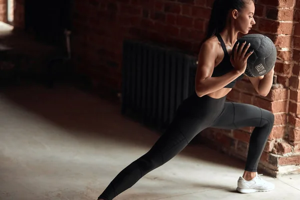 Sportig ung kvinna tränar sqauts med boll i gymmet — Stockfoto