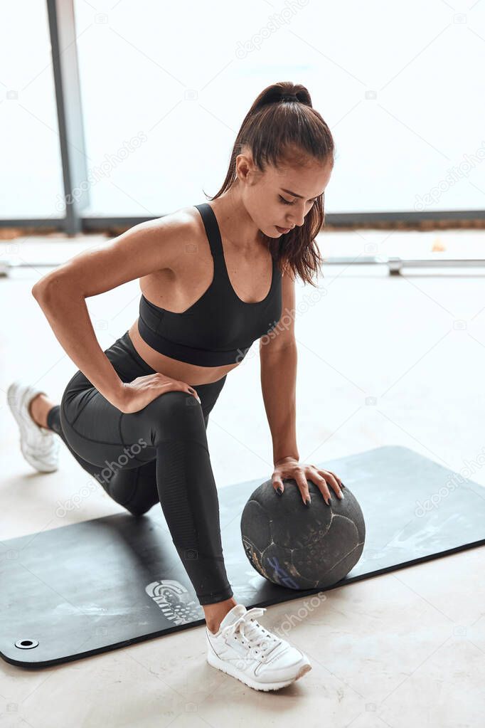 Sport lifestyle. Fit woman in sportsuit stretching legs with medicine ball at gym