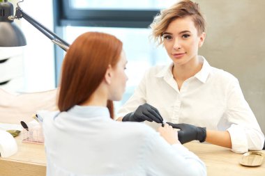 Sevimli ve düşünceli genç bir kadın manikür yapıyor ve kameraya gülümsüyor.