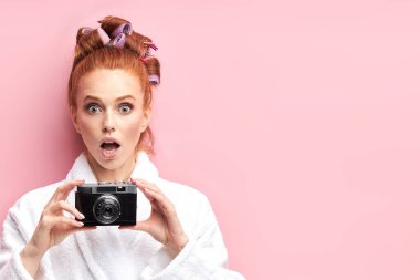 Fotoğraf makinesi olan tatlı kızıl saçlı genç bir kız. Fotoğraf çek. Pembe arka planda izole edilmiş