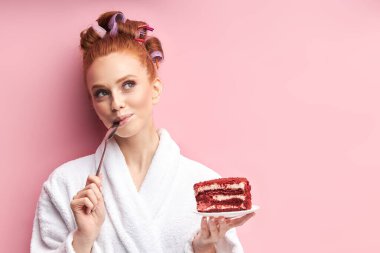 Güzel genç bir kadın pembe arka planda lezzetli pastalar yiyor.