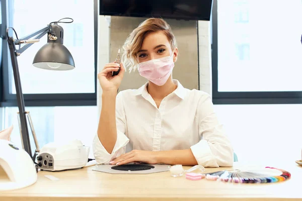 Mooie Kaukasische nagelmeester in masker, manicure zitten voor de camera — Stockfoto