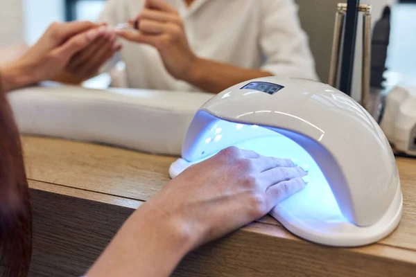 Жінка сушить нігті за допомогою ультрафіолетової лампи з гелевим методом — стокове фото