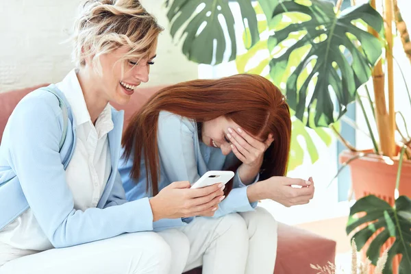 Евфорические жизнерадостные и позитивные девушки смеются, глядя в телефон — стоковое фото