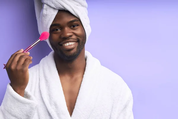 Zabawny Afrykanin noszący szlafrok ze szczotką do makijażu patrzący w kamerę — Zdjęcie stockowe