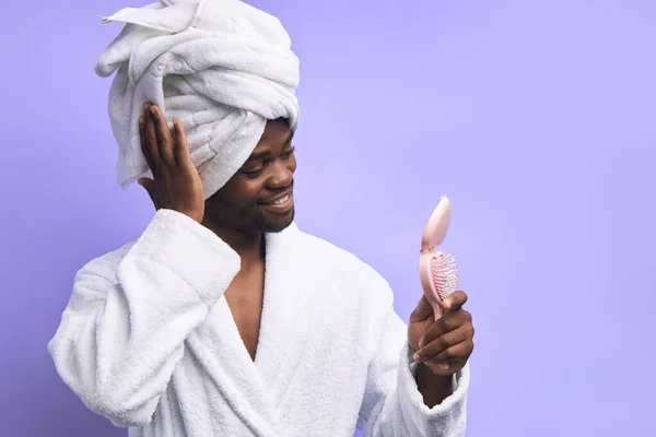 Alegre hombre africano en albornoz y toalla mirando pequeño espejo rosa — Foto de Stock