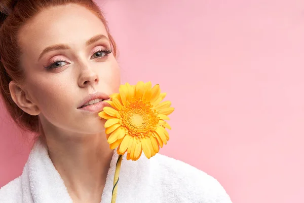 Retrato de una joven hermosa mujer con flores de margarita usando albornoz, aislado sobre fondo rosa — Foto de Stock