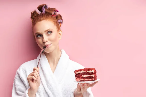 Schöne junge Frau essen leckeren Kuchen auf rosa Hintergrund — Stockfoto